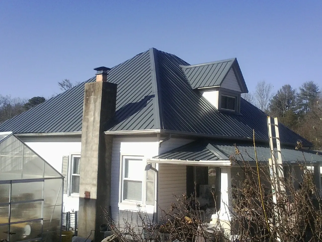 Dark blue standing seam metal roof on a white farmhouse with dormer — Slate & Tile Roof Repair by Roofing Brothers in Schulenburg