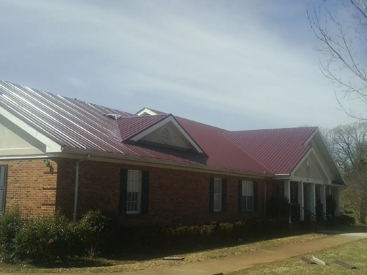 Red metal roof with gabled entries on a long brick building, from a Hail Damage Roof Repair job in Schulenburg