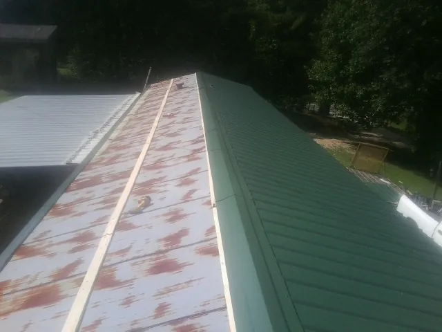 Old rusted panels beside newly installed green metal roofing — Wind Damage Roof Repair by Roofing Brothers in Schulenburg
