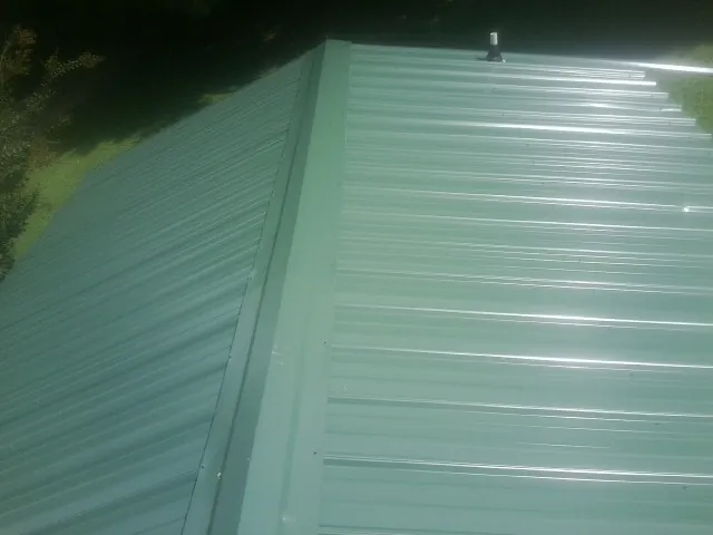 New green metal panels meeting at the ridge of a roof — Flat Roof Repair work by our crew in Schulenburg