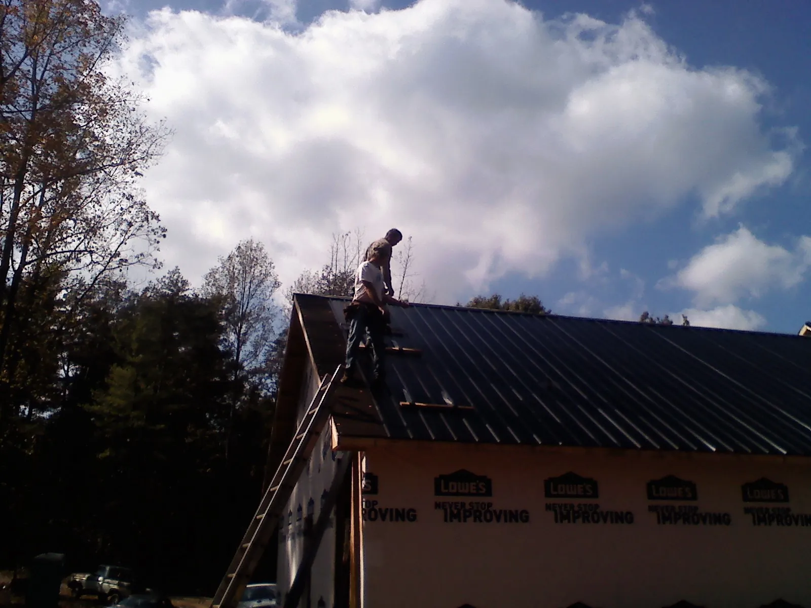 Roofer fastening dark metal panels high against a cloudy sky, from a Roof Inspection job in Schulenburg