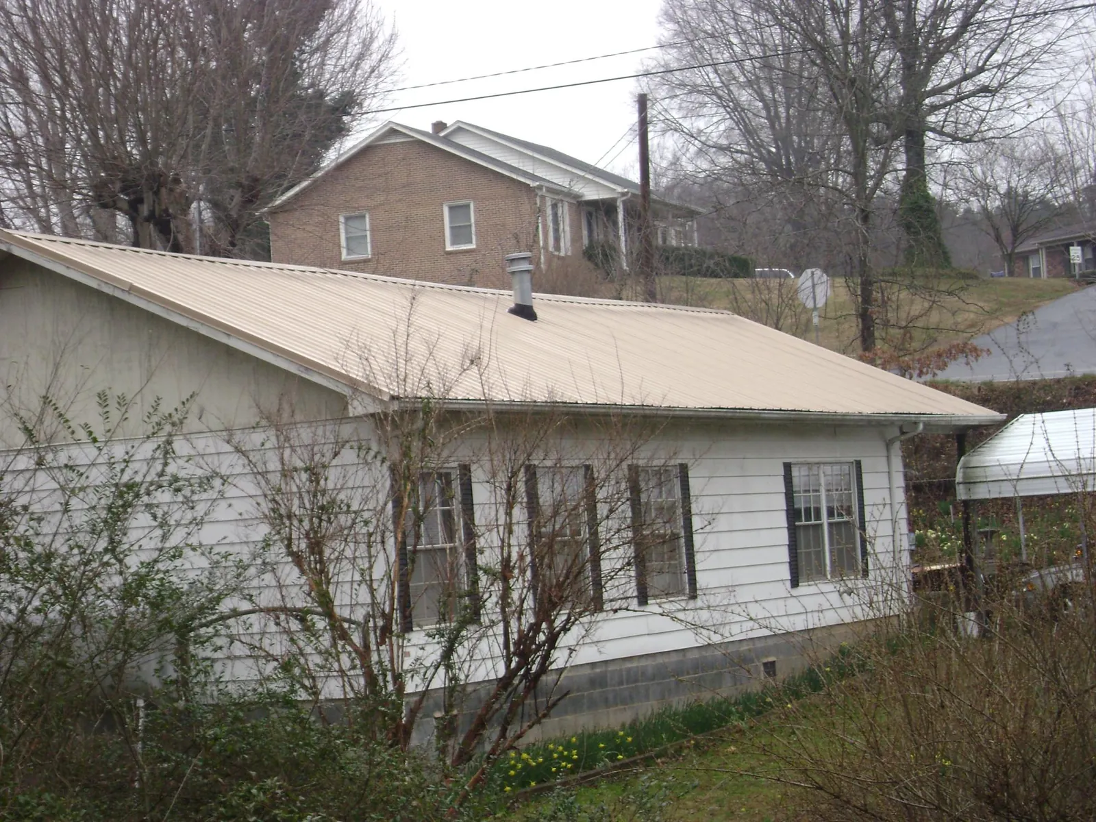 Tan metal roof on a white sided house set into a hillside — Commercial Roofing by Roofing Brothers in Schulenburg
