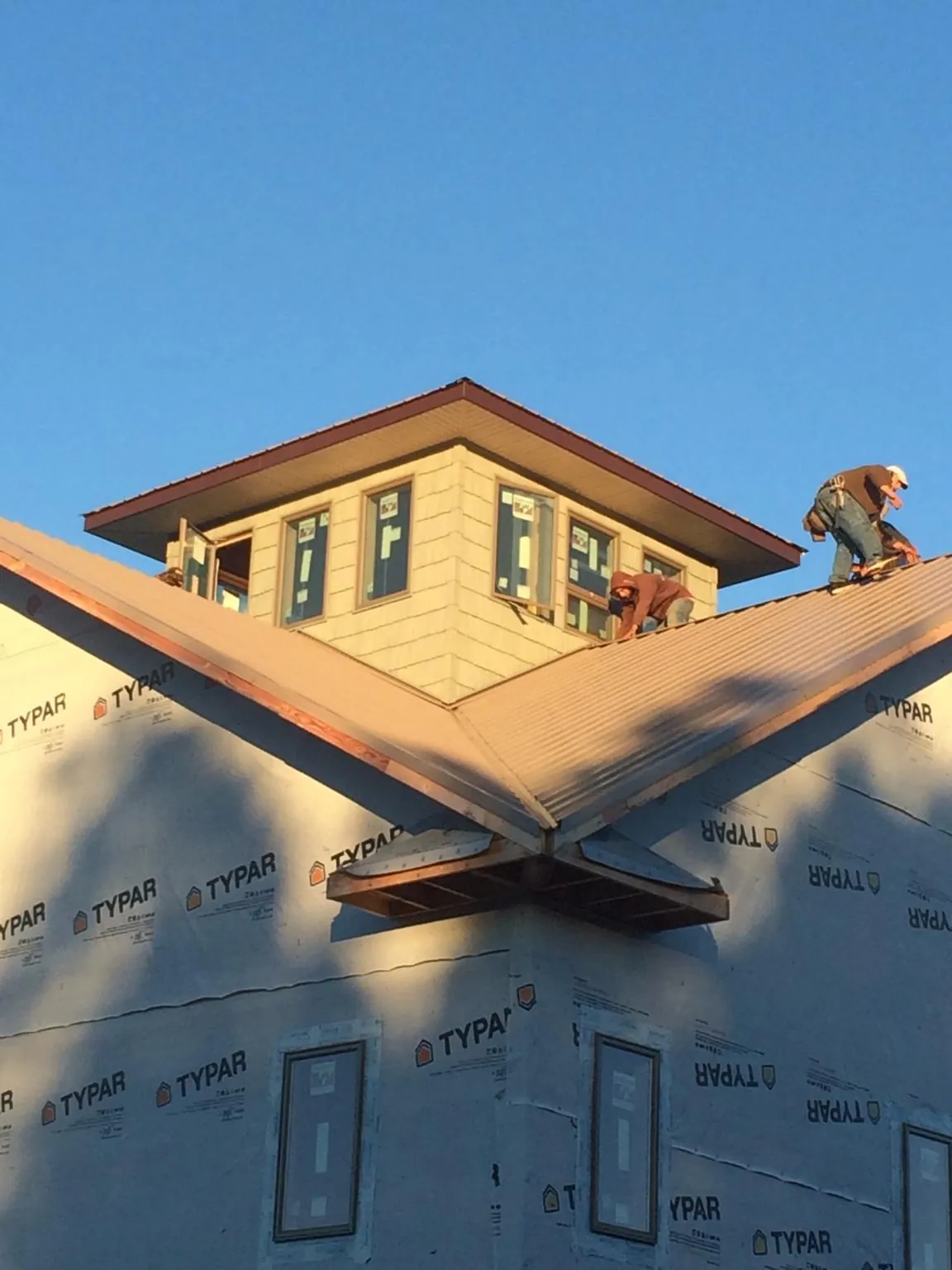 Roofers working around a rooftop cupola on a new metal roof at sunset — Roof Waterproofing in Schulenburg by Roofing Brothers